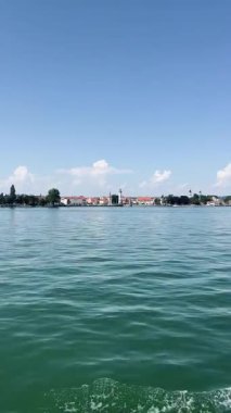Constance Gölü 'nün (Bodensee) dalgalı, yeşil-mavi suları boyunca uzanan geniş panoramik bir manzara uzak kıyı şeridi Lindau' nun pitoresk limanına doğru uzanır.. 