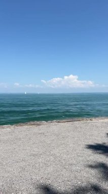Constance Gölü 'nün (Bodensee) dalgalı, yeşil-mavi suları boyunca uzanan geniş panoramik bir manzara uzak kıyı şeridi Lindau' nun pitoresk limanına doğru uzanır.. 
