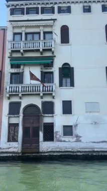 Venedik 'te, çeşitli pencere ve panjurları olan, uzun, eski Venedik binalarıyla çevrili, dar bir kanalın huzurlu manzarası, suyun üzerinde derin gölgeler ve yansımalar yaratır..