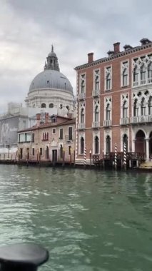 Santa Maria Della Salute Bazilikası 'nın ikonik kubbesi Büyük Kanal' dan Venedik siluetine hükmediyor, tarihi binalar tarafından çevreleniyor ve bulutlu bir gökyüzünün altındaki suya ince yansımalar gösteriyor..