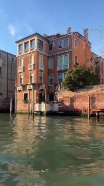 Balkonları ve geleneksel pencereleri olan güzel bir tarihi Venedik sarayı Büyük Kanal boyunca görkemli bir şekilde duruyor. Yansımaları berrak mavi bir gökyüzünün altında suda parıldıyor..