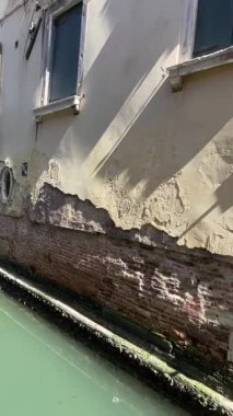 Venedik 'te sakin, dar bir kanal yıpranmış cepheleri, kemerleri ve parlak gökyüzünün altında küçük bir köprüsü olan tarihi binalar arasında akar..