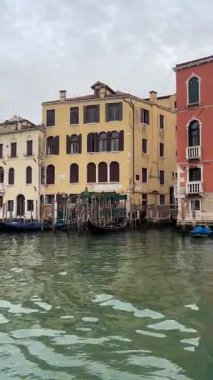Venedik 'teki Büyük Kanal' ın klasik bir sahnesi. Kapalı bir gökyüzünün altında, tarihi sarı bir sarayın önüne demirlemiş geleneksel gondollar..