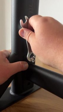 Duvara monte edilmiş bir barfiks çubuğunun siyah metal çerçevesini sıkmak için bir ingiliz anahtarı kullanan birinin ellerinin yakın çekim görüntüsü, montaj aşamasında ayrıntılı bir adım olduğunu gösteriyor..