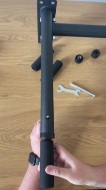 Duvara monte edilmiş bir barfiks çubuğunun siyah metal çerçevesinde sürgüyü sıkarken, ingiliz anahtarı ve ahşap bir yüzey üzerindeki diğer parçalarla....