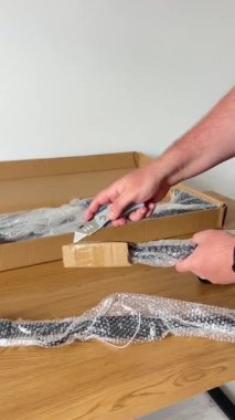 Çekme çubuğunun karton ambalajını açmak için kullandıkları alet bıçağını kullanarak, baloncuklu metal bileşenleri açığa çıkaran bir kişinin yakın plan fotoğrafı..