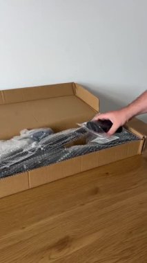 Bir el, ambalajdan yeni çıkarılmış iki siyah köpük sapına uzanır, içinde tahta bir yüzey üzerinde diğer çekiş çubuğu bileşenleri olan açık bir karton kutunun yanında..