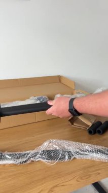 Yeni bir barfiks çubuğunun birkaç siyah metal bileşeni. Koruyucu baloncuk ambalajından yeni çıkarılmış. Tahta bir yüzeyde, açık karton kutunun yanında duruyor..