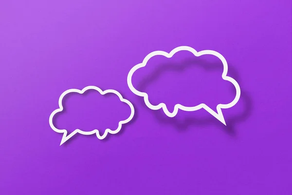 White paper cut out speech bubble shapes set on purple paper background.