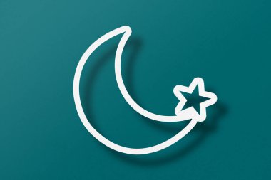 White paper cut into crescent shapes and stars set on green paper background.