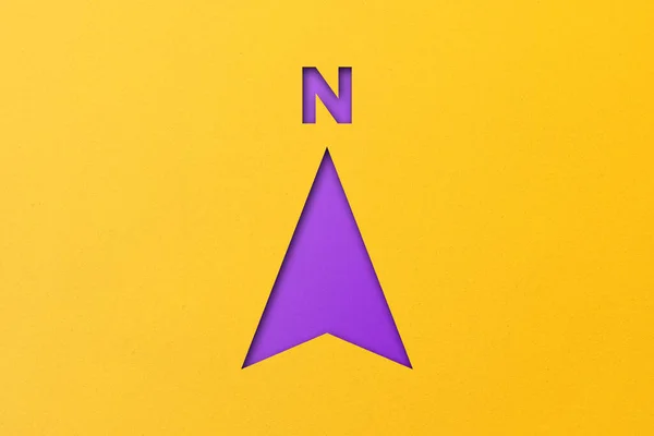 以黄色纸为背景的北方箭头形状的紫色剪纸 — 图库照片