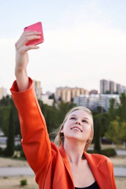 Günlük giysiler içinde güzel gülümseyen bir manken. Sokakta poz veren kaygısız bir kadın. Akıllı telefondaki selfie oto portre fotoğrafları.