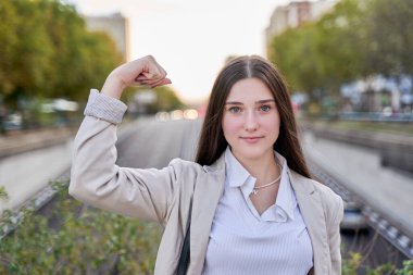 İş kıyafetleri giymiş genç İspanyol kız gururla gülümseyen kol kaslarını gösteriyor. fitness konsepti.