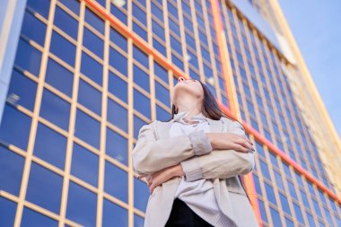 Kollarını kavuşturmuş genç bir iş kadını. Kafkasyalı, uzun saçlı, yukarı bakıyor.