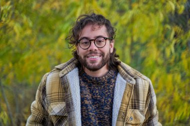 Yeşil ağaçlarda sakallı ve gözlüklü bir trans adamın portresi.