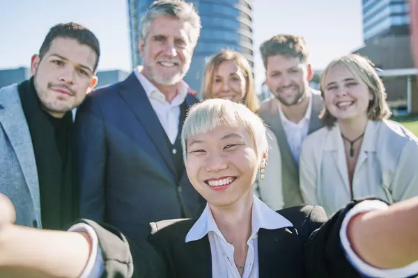 Multicultural community of people smiling together at camera - Happy diverse business people taking selfie picture with smart mobile phone device - Friendship and human relationship concept