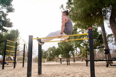Spor giyinen bir adam spor salonunda paralel barları kullanarak antrenman yapıyor.