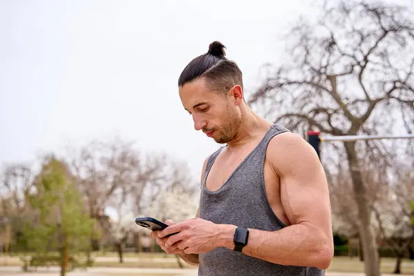 muscular man in a training park looking at his smart phone