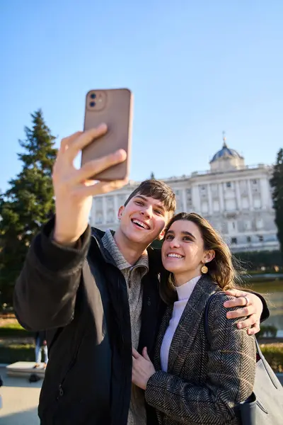 young couple visiting the royal palace in Madrid taking a selfie with their smartphones