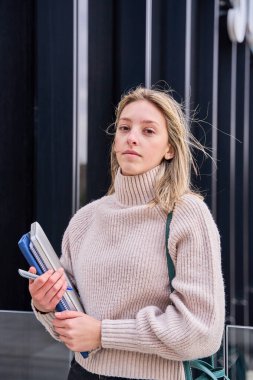 Elinde defterler ve kitaplarla kameraya bakan genç bir kız öğrencinin portresi.