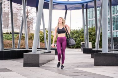 Spor yapmak için spor salonuna giderken sırt çantasıyla yürüyen genç bir kadın. Şehirdeki koşuşturma ve koşuşturmadan kopan kadın spor yapmaya koyuldu..