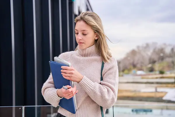 portrait of a blonde woman in casual clothes holding a folder and a work computer in her arms. education and business concept