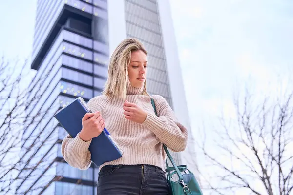 portrait of a female university student with books and notebooks in her hand standing on the university campus.