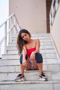 Genç Latin, merdivenlerde oturmuş kameraya bakıyor.