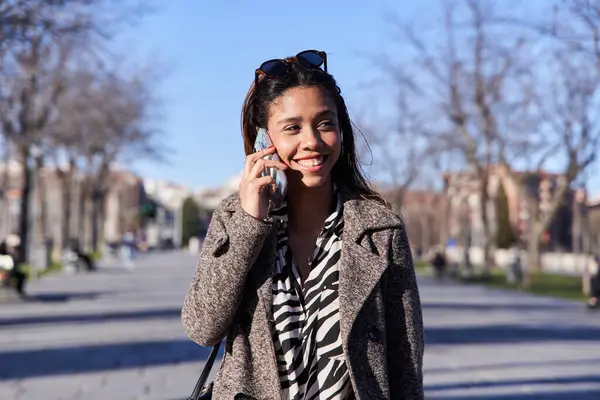 young latina woman talking on smartphone walking in the city.