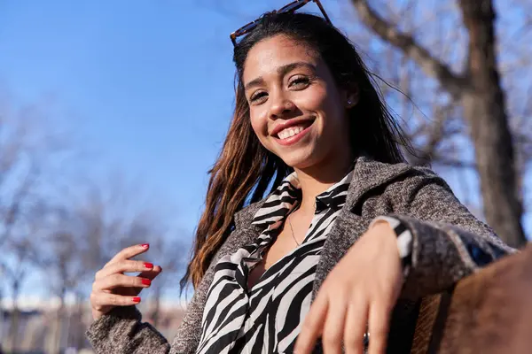 young latina sitting on a bench looking at the camera with a perfect white smile