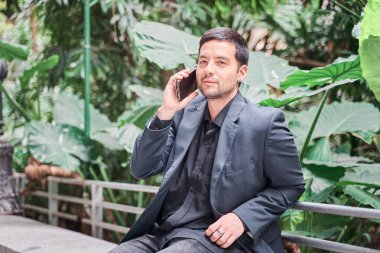 Takım elbiseli genç Latin adam iş telefonuyla konuşuyor.