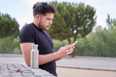 Alıştırma yapmaya ara verirken akıllı telefonuna bakan çekici Latin adam.