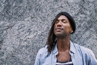 Gri duvar ve gözlerin önünde dikilmiş, şık bereli yakışıklı Afro-Amerikalı adam gözlerini kaçırıyor.