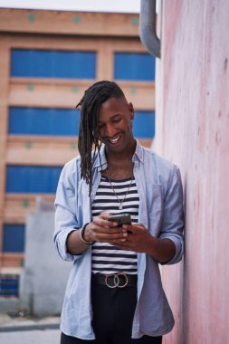 Kafasında örgüler olan genç Karayipli adam akıllı telefonunu şehirde kullanıyor.