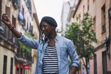 Siyah saçlı, bereli, neşeli ve gözleri kapalı bir şekilde şehrin ortasında elini kaldıran Afro-Amerikan bir adam..