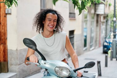 Kıvırcık saçlı bir adamın portresi. Kocaman bir gülümsemeyle motosikletine biniyor.