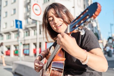 Albümünü tanıtmak için şarkı söyleyen ve gitar çalan genç bir kadın şarkıcı-söz yazarı..