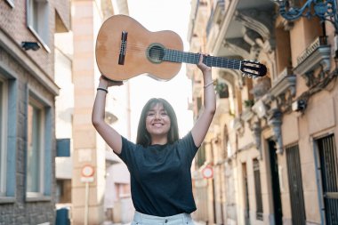 Klasik gitarı kafasının üzerine kaldıran genç bir Latin kadının portresi.