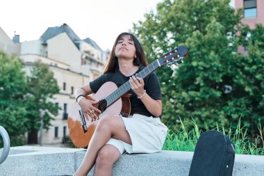 Arka planda, gitar çalan ve şehirle şarkı söyleyen Latin bir kadının portresi.