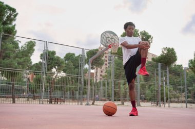 Genç Afro-Amerikalı basketbolcu oynamadan önce bacaklarını açıyor.