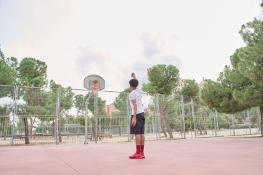 Genç basketbolcu, sahada antrenman yaparken basket atıyor.