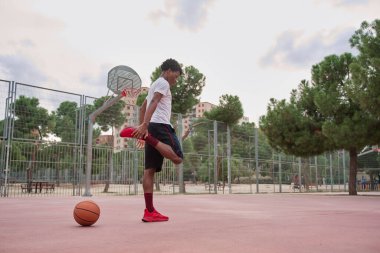 Genç Afro-Amerikalı basketbolcu oynamadan önce bacaklarını açıyor.