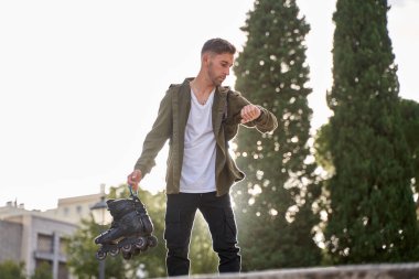 Şehir kıyafetleri içindeki sportif adam elinde paten olan saate bakıyor.