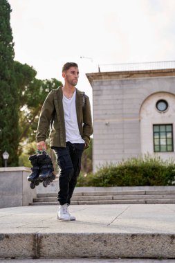 Elinde bir çift paten olan genç bir adamın dikey fotoğrafı..