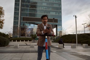İş adamı akıllı telefonunu scooterında kullanıyor. yeşil ulaşım aracı