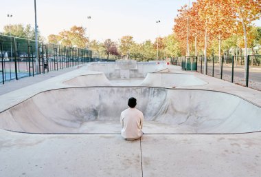 Tanımlanamayan bir adam rampada oturmuş boş bir kaykay parkına bakarken düşünüyor.
