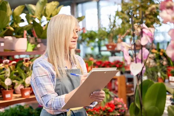 Çocuk odasında çalışan orta yaşlı bir kadın. Defterde envanter tutuyor. Çiçekçide çalışan orta yaşlı bir kadın..
