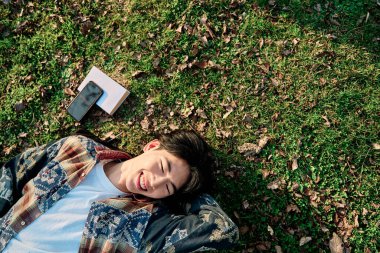 Asyalı bir adamın portresi çimenlikte uzanan kameraya bakıyor bir kitap ve metin için kopyalama alanı var..