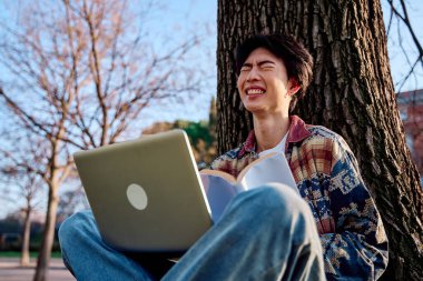 Dizüstü bilgisayarında çalışan Asyalı bir adam modern bir öğrencinin özünü sergiliyor..