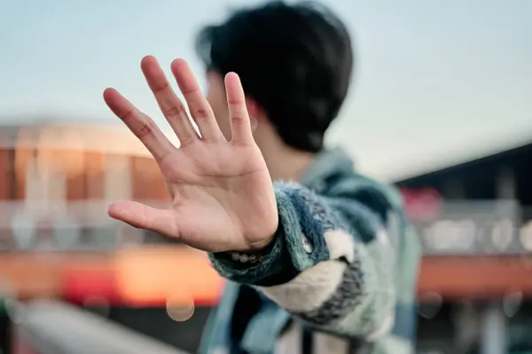 stock image young asian man covering his face in a stop sign. young celebrity covering his face with the palm of his hand and looking away to avoid paparazzi.